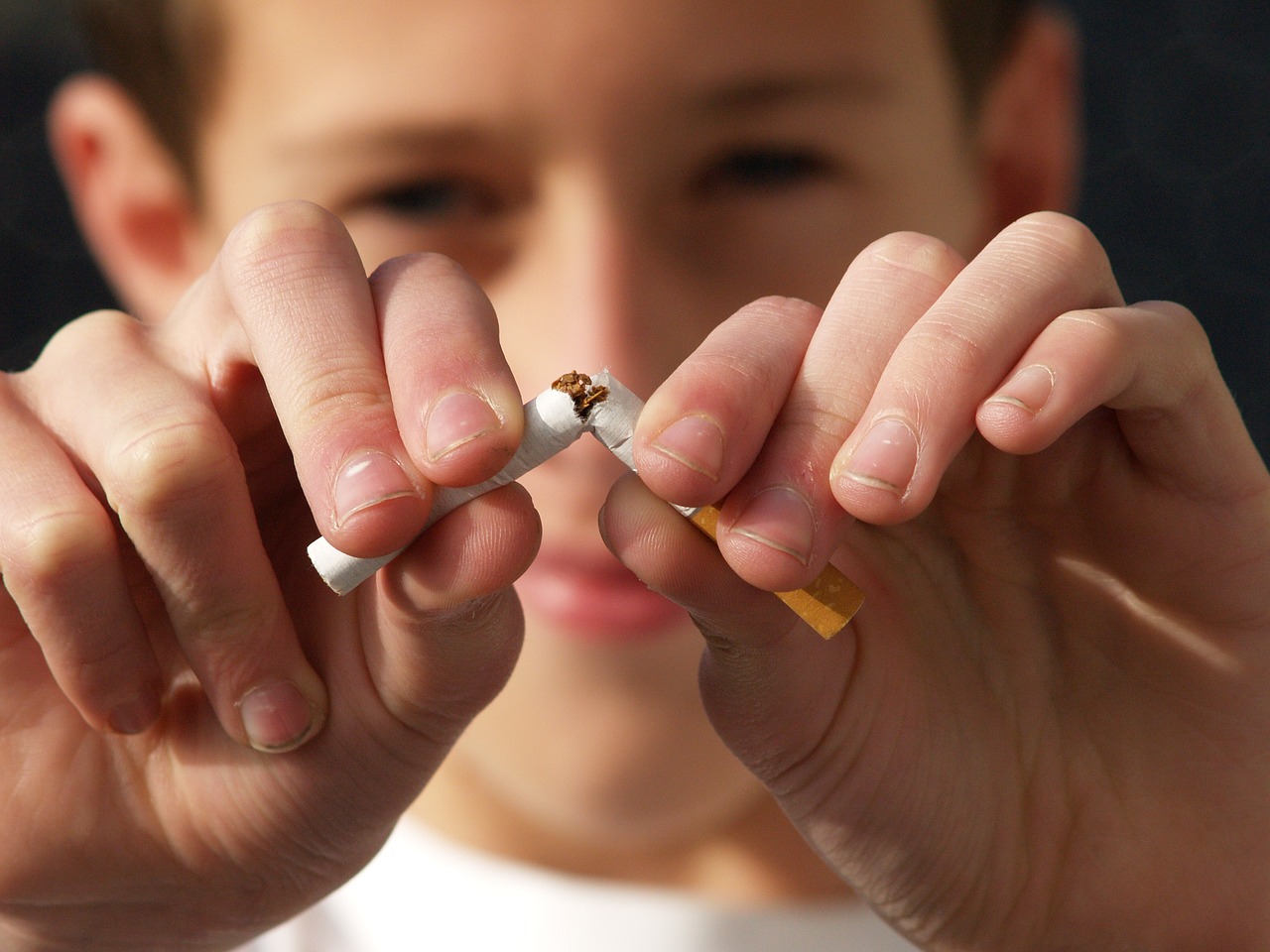 A young boy breaking a cigarette stick.